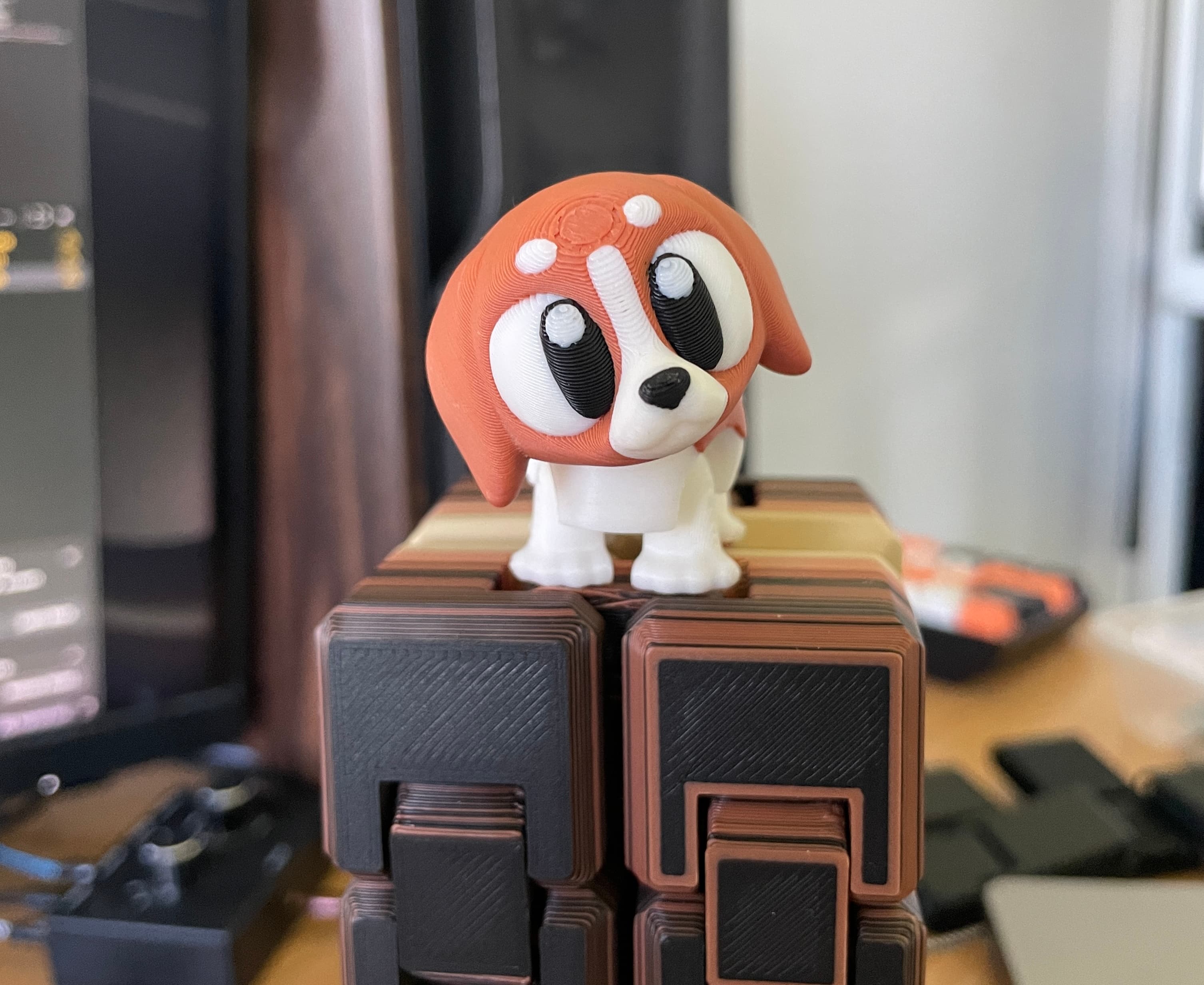 Orange and white 3D-printed puppy toy sitting on stacked brown cubic blocks on a desk
